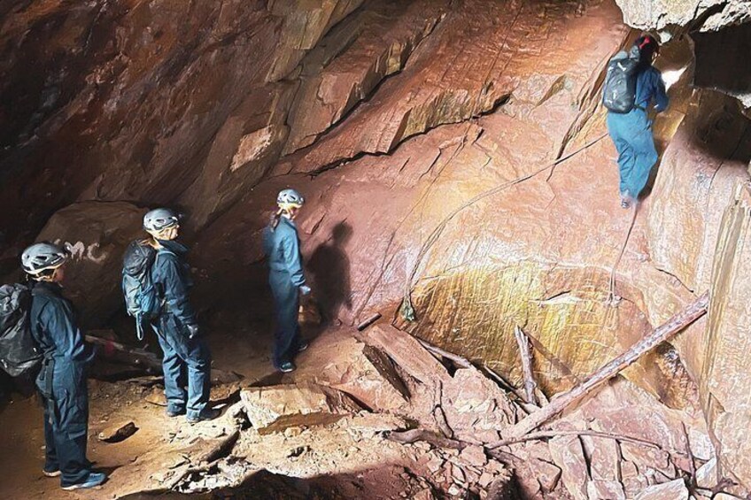 A group of people in protective gear exploring a cave with rocky walls and a large boulder. 3