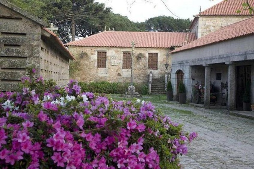 A courtyard with stone buildings, a cobblestone path, and flowering bushes. 1