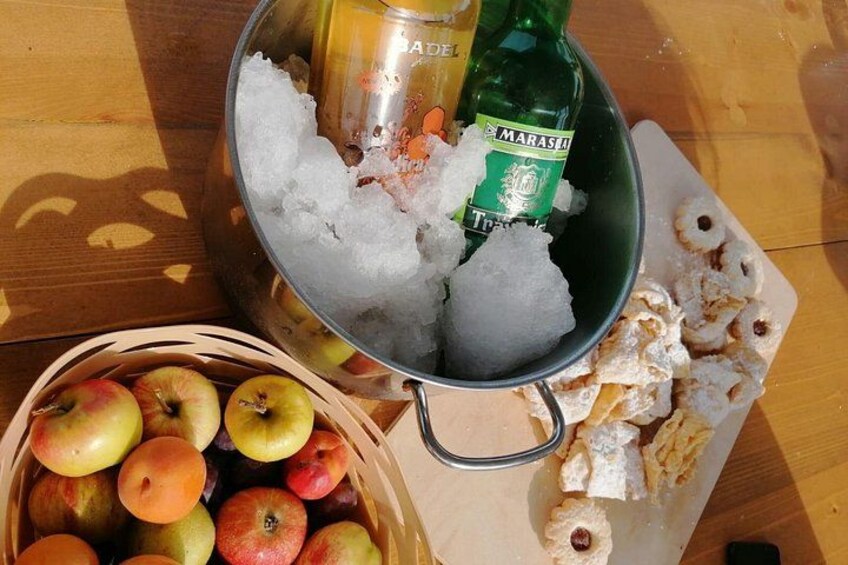 A metal bowl filled with ice, a bottle of beer, a basket of apples, and a cutting board with pastry. 3