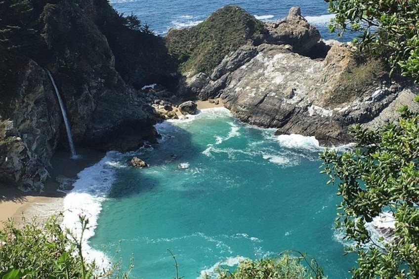 A coastal landscape with a waterfall, rocky cliffs, and turquoise waters. 4