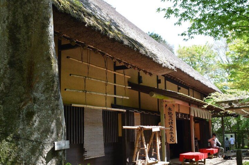 A traditional Japanese building with a thatched roof, wooden beams, and a red table outside. 1