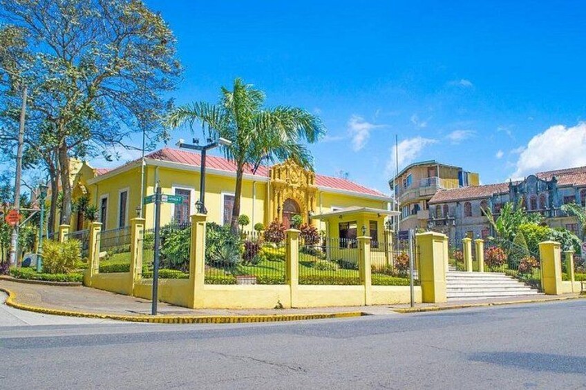 Un edificio amarillo con techo rojo, rodeado de vegetación y una cerca. 2