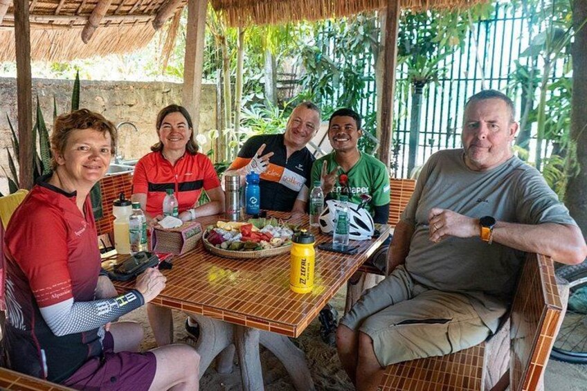 Un grupo de personas sentadas en una mesa al aire libre, con comida y bebidas, rodeadas de vegetación. 4
