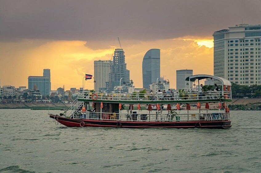 Un barco de paseo fluvial con pasajeros, el perfil urbano de una ciudad y una puesta de sol. 2