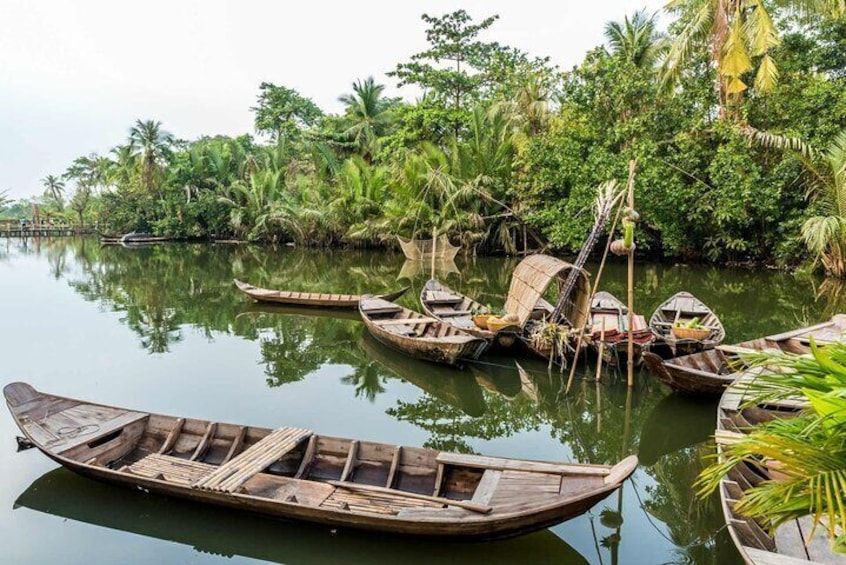 Een rustige rivier met verschillende traditionele houten bootjes die aan de oever liggen, omgeven door weelderige begroeiing en palmbomen. 3