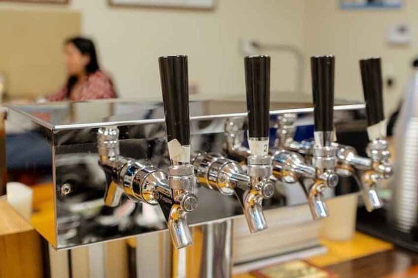 A row of beer taps with black handles on a stainless steel counter. 5