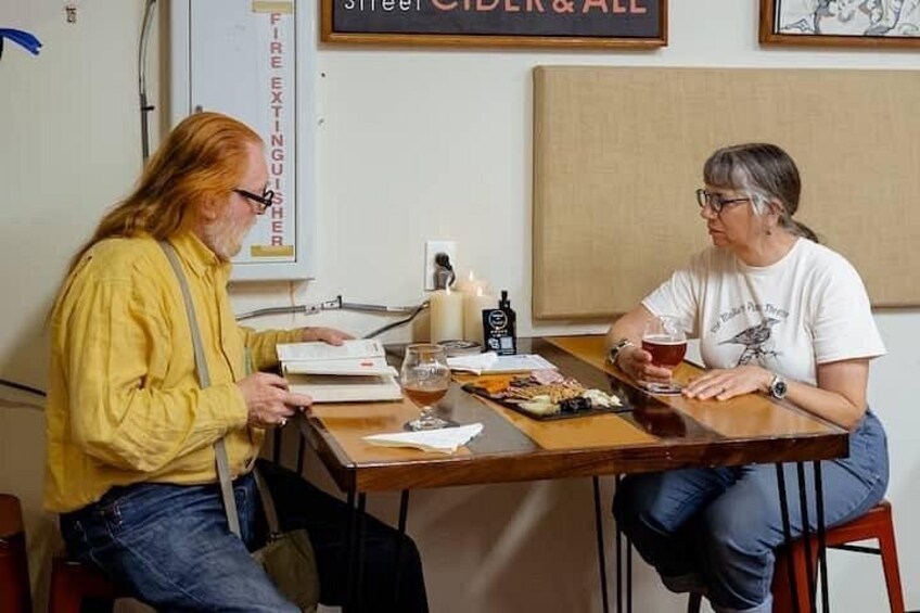 Dos personas sentadas en una mesa de madera con un menú, una vela y una botella de licor. 1