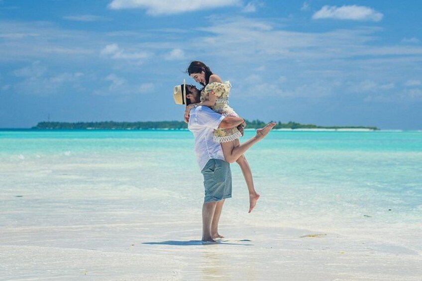 Une personne portant une autre sur ses épaules, sur une plage bordée d’une eau turquoise et transparente, avec une île visible au loin. 1
