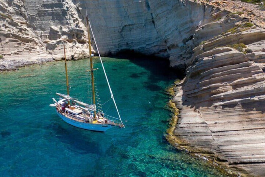 A sailboat anchored near a rocky coastline with clear blue water. 4