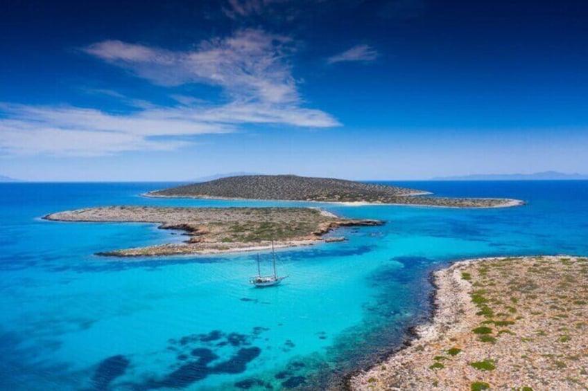 A clear blue sea with a sailboat, a rocky coastline, and a distant island. 3