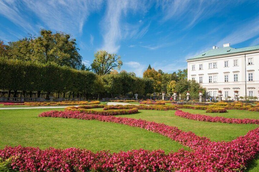 A formal garden with geometric flower beds and a large building in the background. 5
