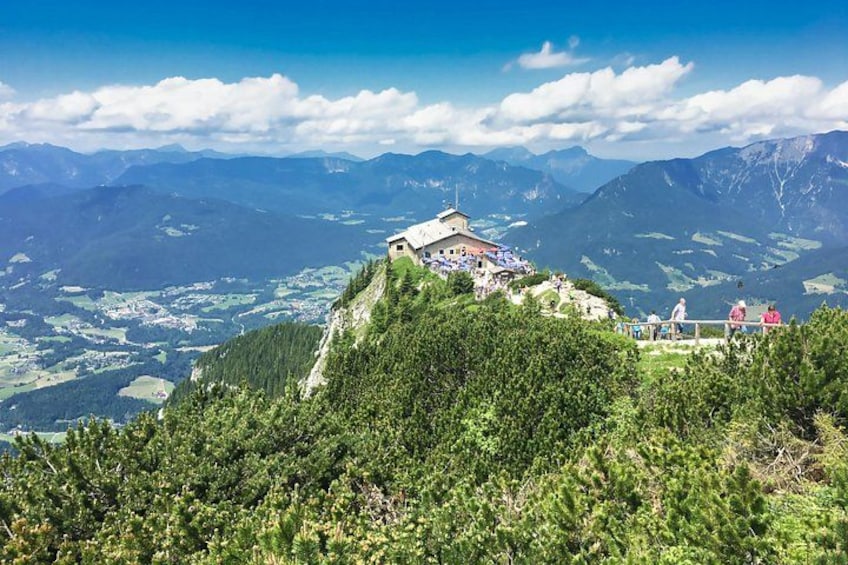 A mountain peak with a small building, lush greenery, and a valley below. 1