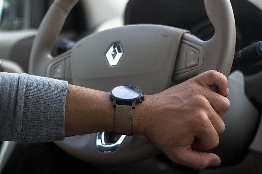 A person's hand on a car steering wheel with a watch on their wrist. 2