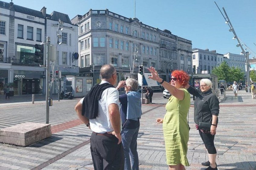 A group of people standing on a city sidewalk with buildings in the background. 1