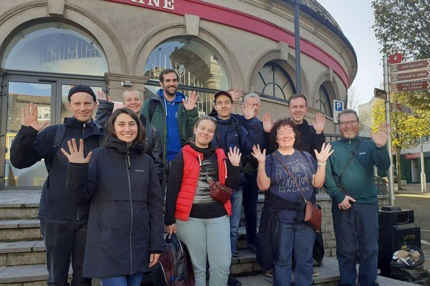 A group of people posing in front of a building with a circular facade and a sign indicating directions. 3