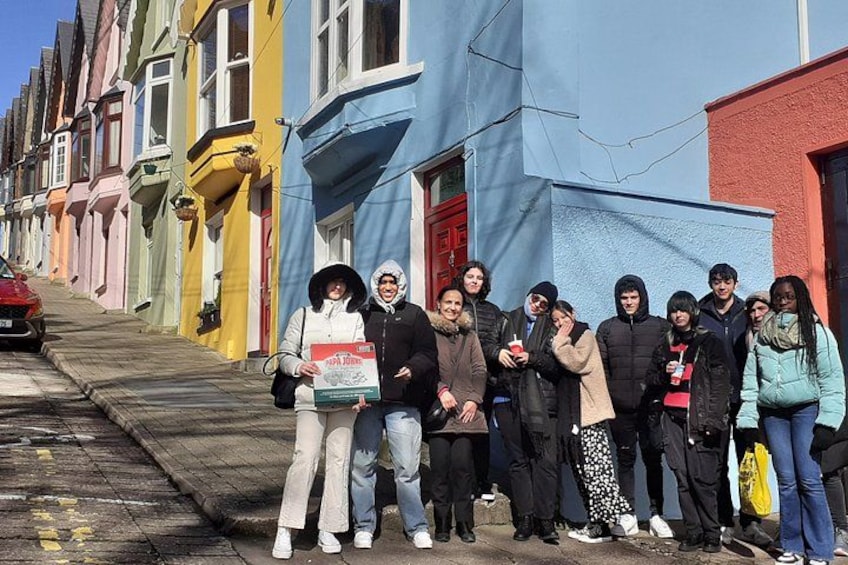 A group of people standing on a street with colorful houses. 2
