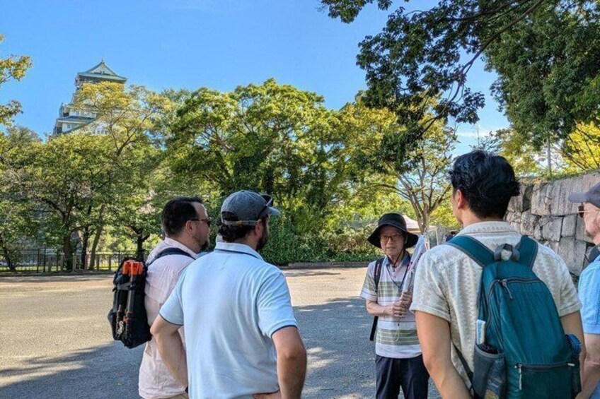 Un groupe de personnes se tient à l’extérieur, certaines avec des sacs à dos, et observe un bâtiment éloigné qui présente un style architectural traditionnel. 2