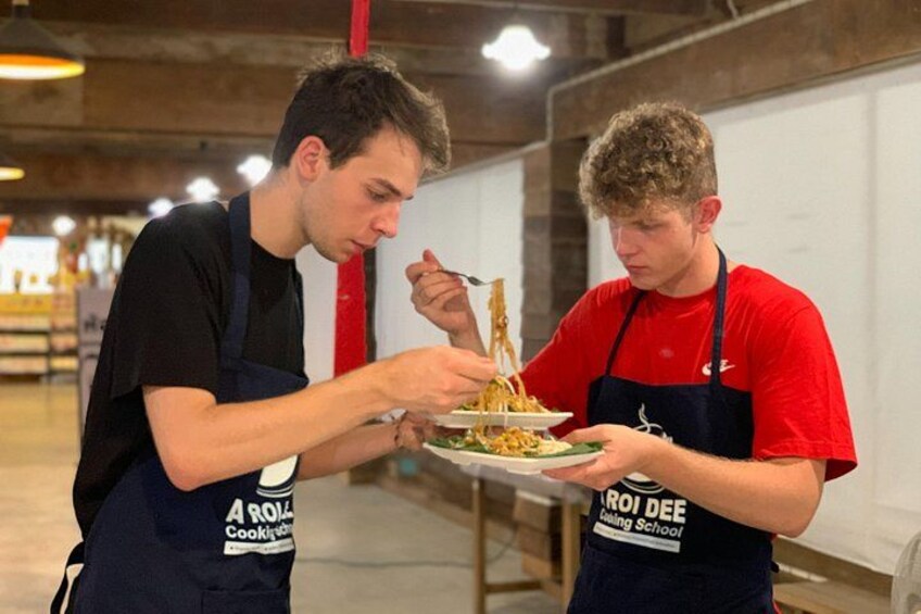 Due persone con grembiuli con loghi mangiano da piatti in una cucina. 5