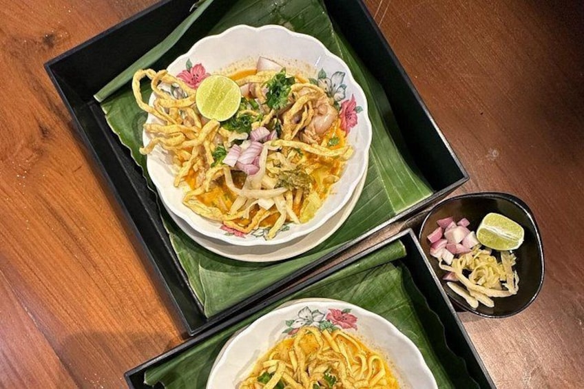 Una ciotola di noodles con condimenti e un spicchio di lime su un vassoio di foglie di banano. 3