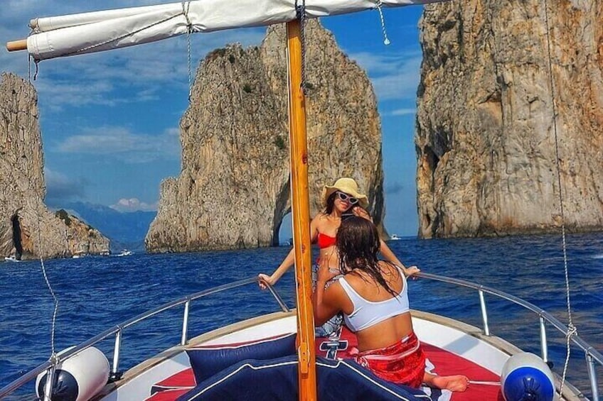 A boat with two people wearing hats and sunglasses, sailing near rocky cliffs. 1