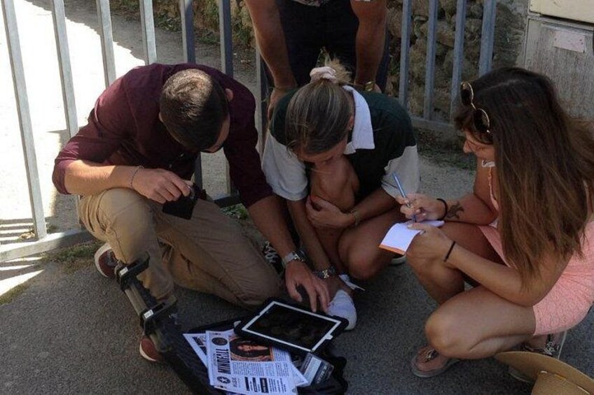 A group of people sitting on the ground, examining a tablet and some papers. 2