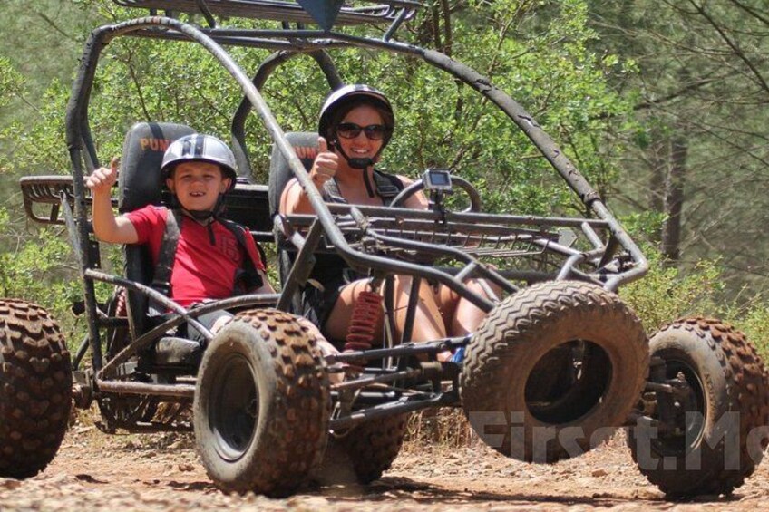A person in a buggy with large off-road tires, steering wheel, and a seatbelt. 5