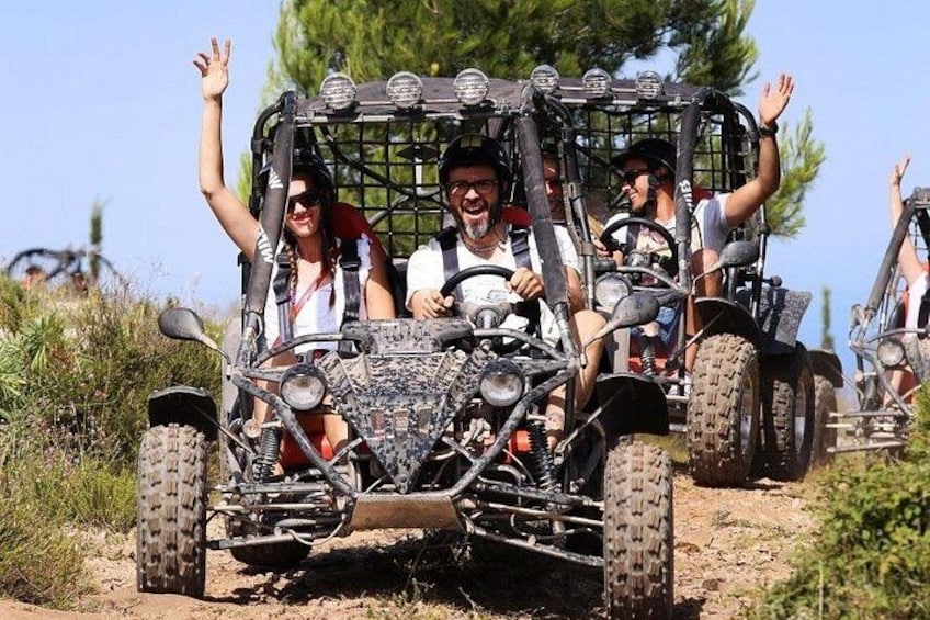 A quad bike with four passengers, one raising an arm, on a dirt path surrounded by greenery. 4