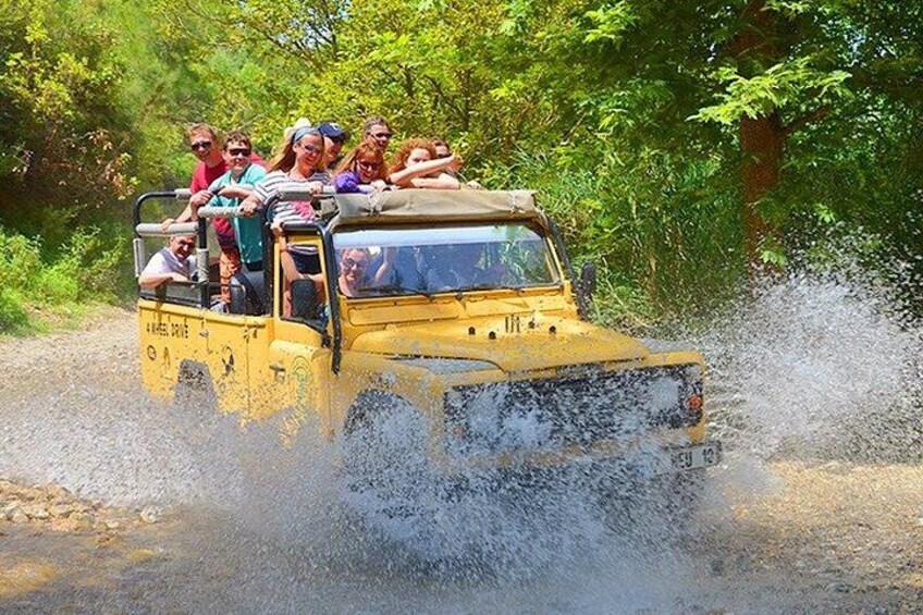 A yellow off-road vehicle driving through a shallow water crossing, with passengers visible. 3