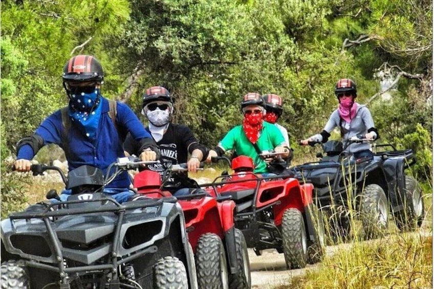 Four people riding ATVs on a trail surrounded by trees. 2