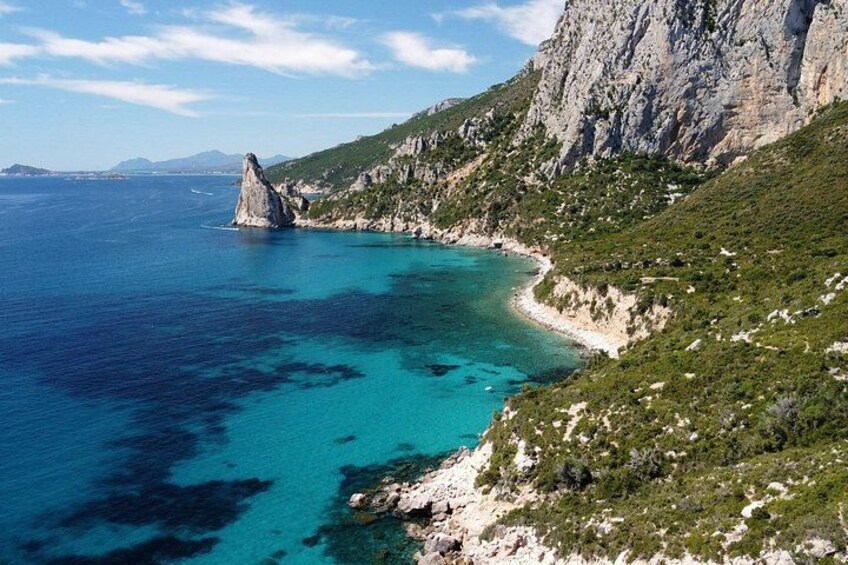 A coastal landscape with clear turquoise waters, a rocky outcrop, and a mountainous backdrop. 3