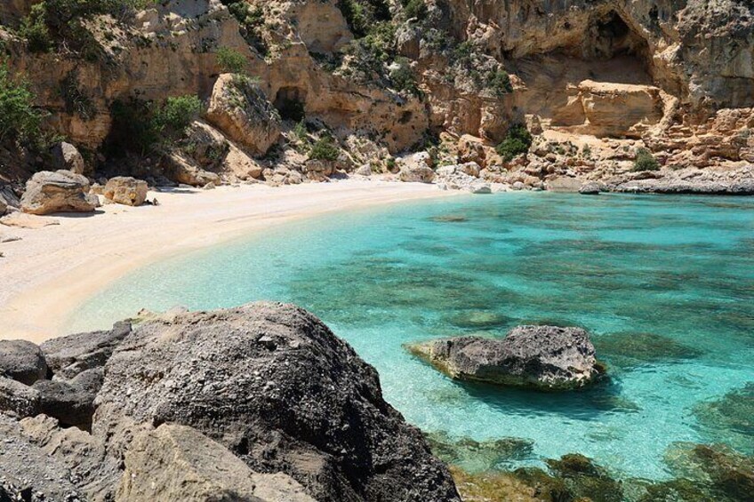 A beach with clear turquoise water, rocky outcrops, and a sandy shore. 3