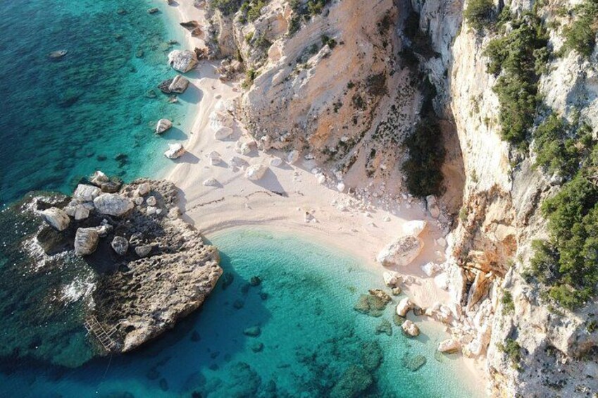 A coastal landscape with clear turquoise waters, a sandy beach, rocky outcrops, and a steep cliff. 4