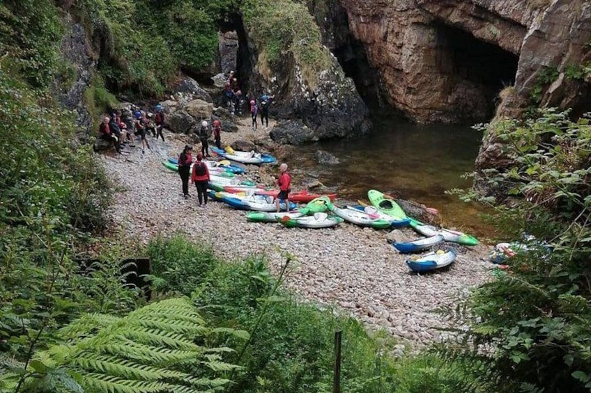 A group of people near a rocky riverbank with kayaks lined up. 1
