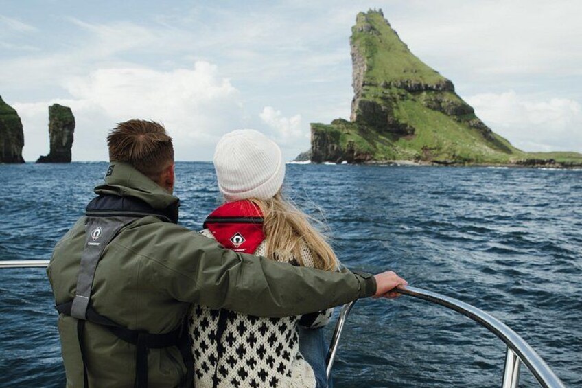 A couple on a boat with a green island and rocky outcrops in the background. 5