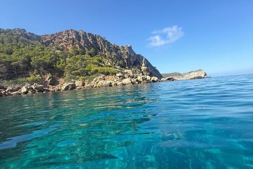 A coastal landscape with clear turquoise waters, rocky cliffs, and dense green vegetation. 4