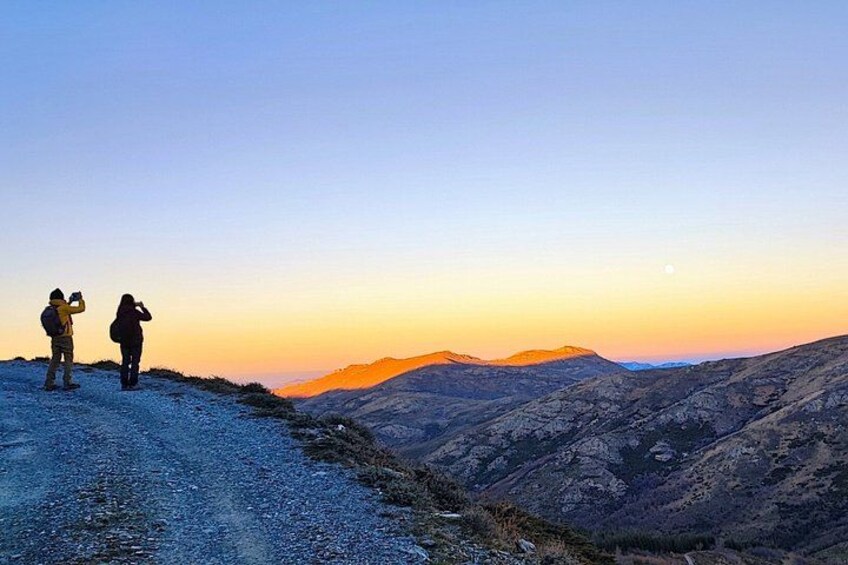 Two people standing on a mountain ridge during sunset. 1
