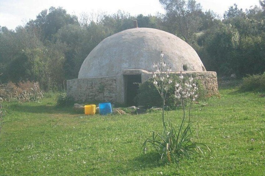 A stone dome structure in a grassy field with a clear sky. 2