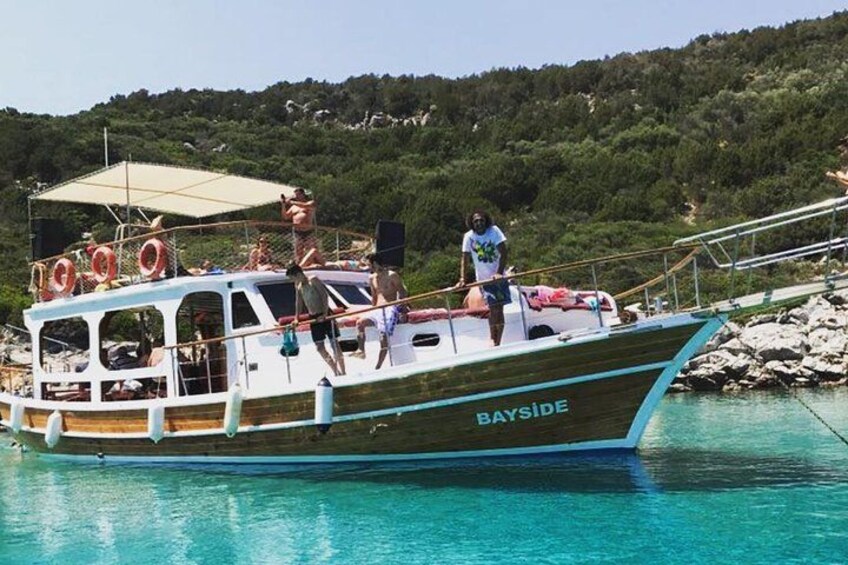 A boat named 'BAYSIDE' docked at a harbor with clear turquoise water and a forested hill in the background. 5