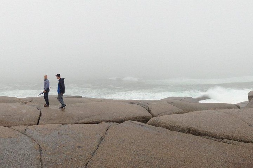 Two people walking on rocky terrain near a turbulent sea. 2