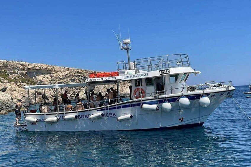 A boat named 'TAMENA BOAT SERVICES' with people on board, anchored near rocky coastline. 3