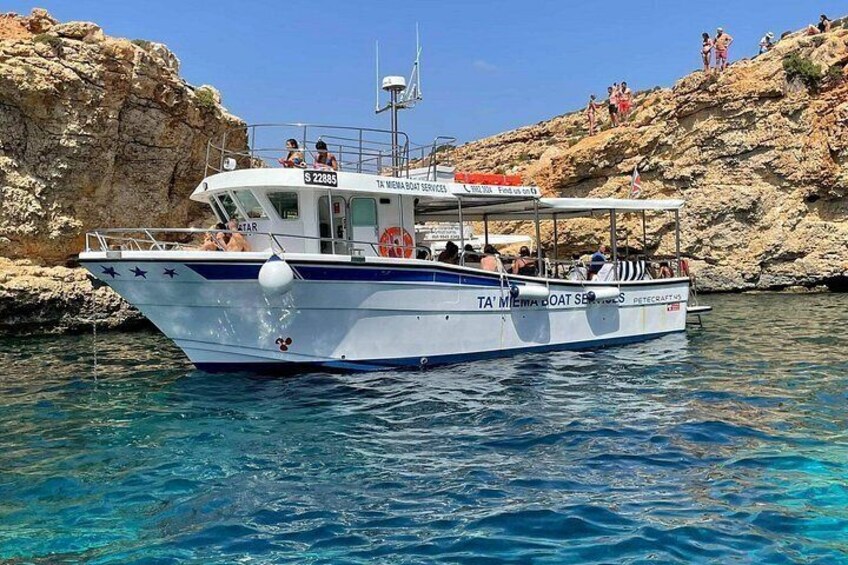A boat named 'TA' MENA BOAT SER' with people on board, anchored near rocky cliffs. 1