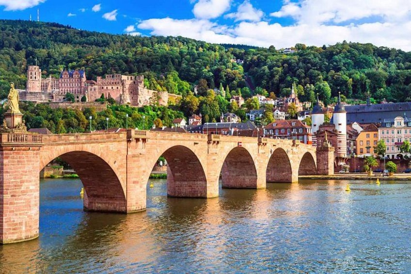 A stone bridge with multiple arches over a river, a statue on the bridge, and a castle on a hill in the background. 1