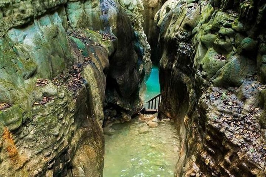 A narrow rocky gorge with a turquoise pool and a wooden staircase leading down. 3