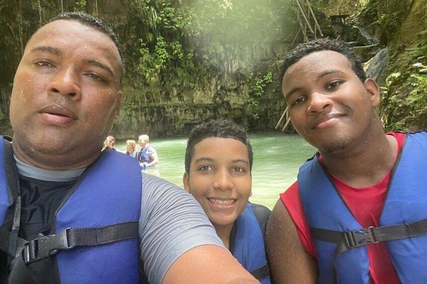 Three people wearing life jackets near a river with a rocky background. 2