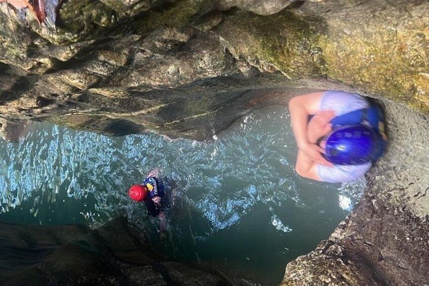 A person in a red helmet and blue wetsuit swimming in a rocky water body. 1
