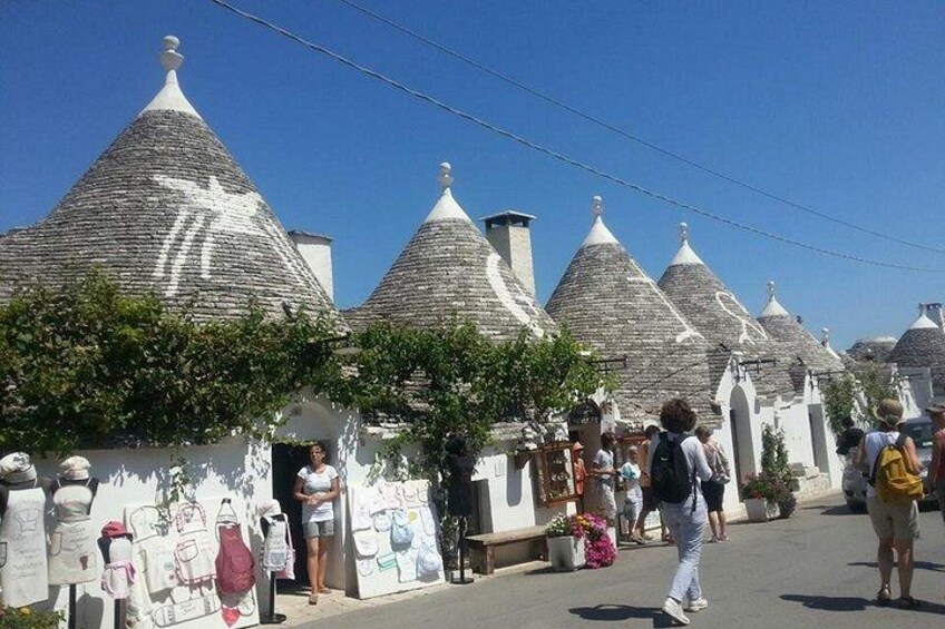 Eine Straße gesäumt von traditionellen Gebäuden mit Stein-Dächern, eine Menschenmenge und ein klarer, blauer Himmel. 2