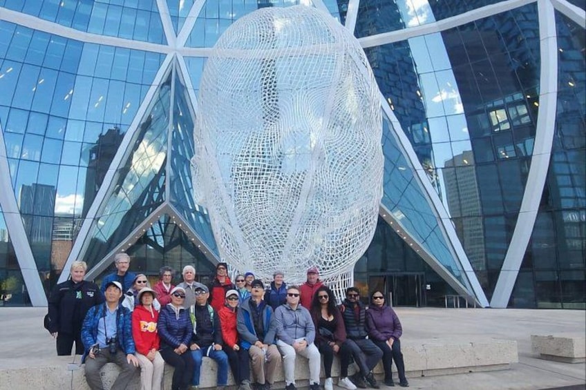 A group of people sitting in front of a modern glass building with a large spherical sculpture. 4