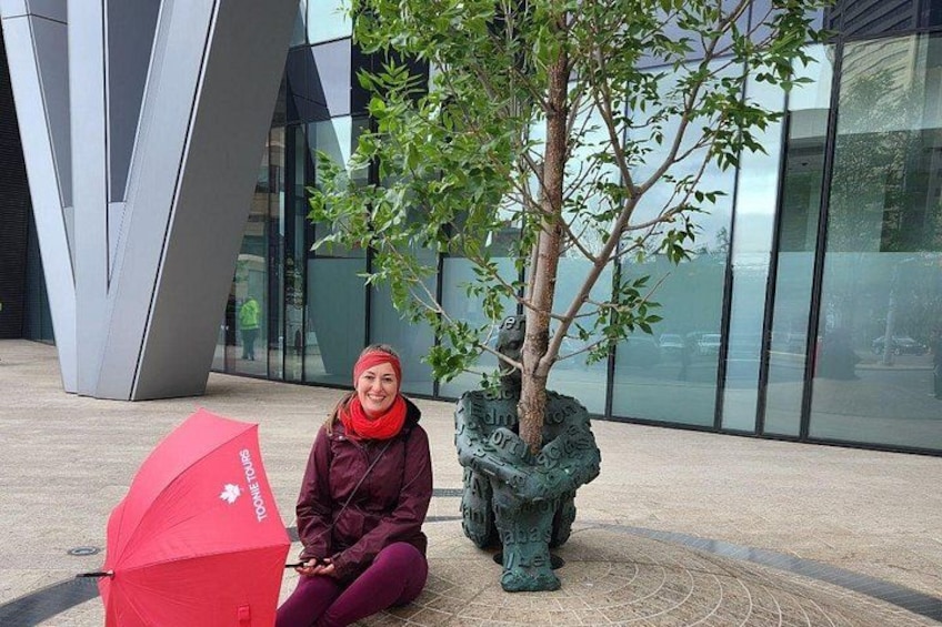 A person sitting on the ground next to a tree and a red umbrella. 2