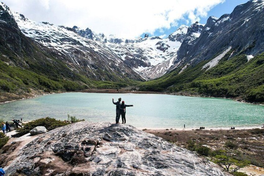 Une personne se tient debout sur un promontoire rocheux, surplombant un lac turquoise entouré de montagnes. 2