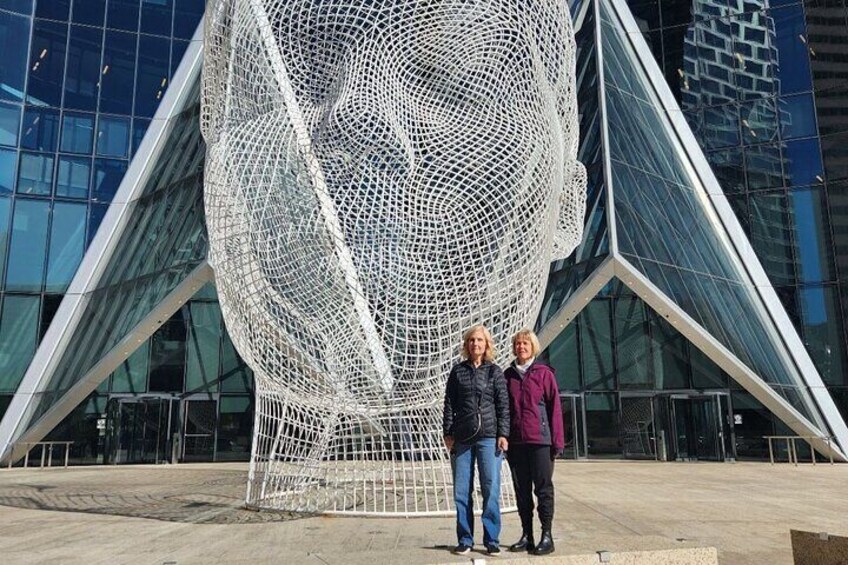 Two people standing in front of a large, geometric sculpture. 1